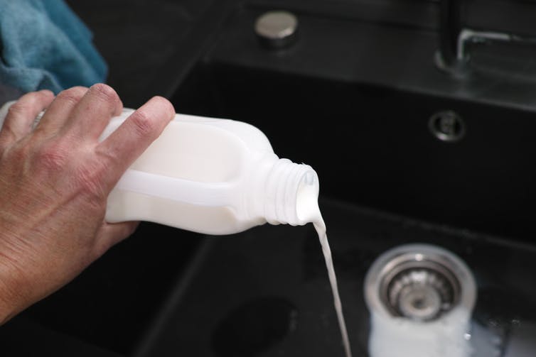 A hand pours a bottle of milk down the sink.