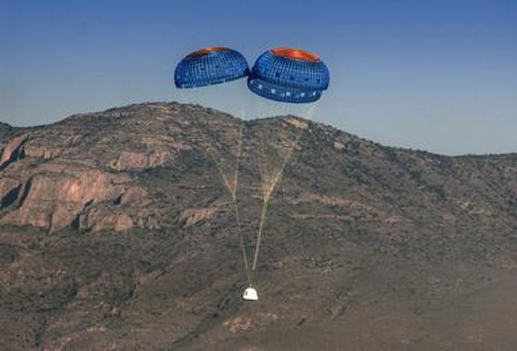 Image of Blue Origin's New Shepherd spacecraft landing with parachutes.