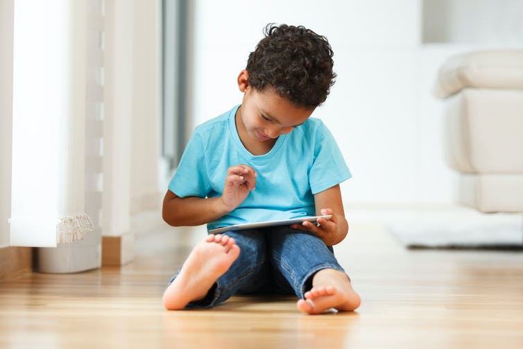 A young boy sitting on the floor using a tablet.