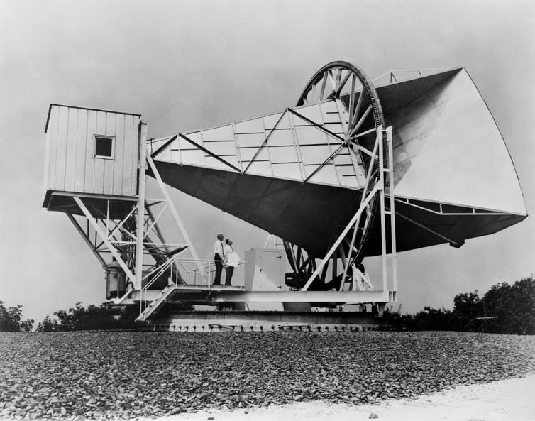 Black and white image of antenna equipment with two men standing on it