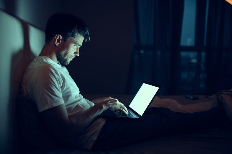 Man in bed looks at laptop