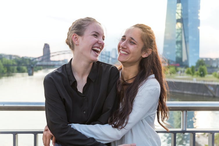 Two young women standing on a bridge laughing together.